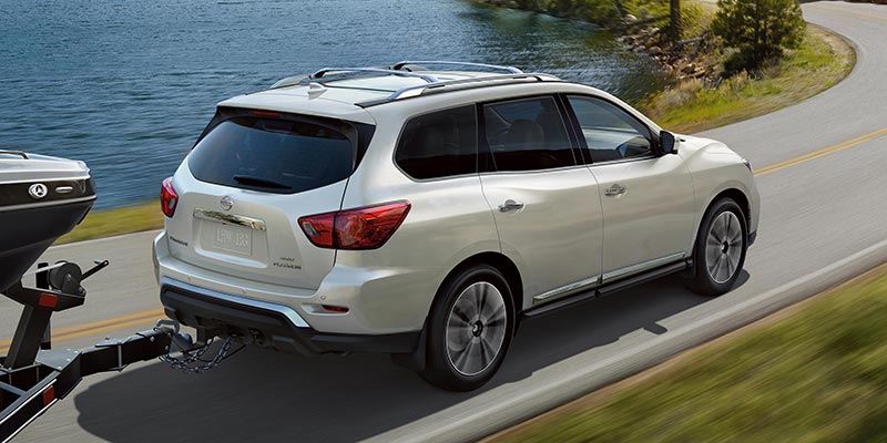 SUV towing a boat on a trailer, driving on a winding road next to a lake.